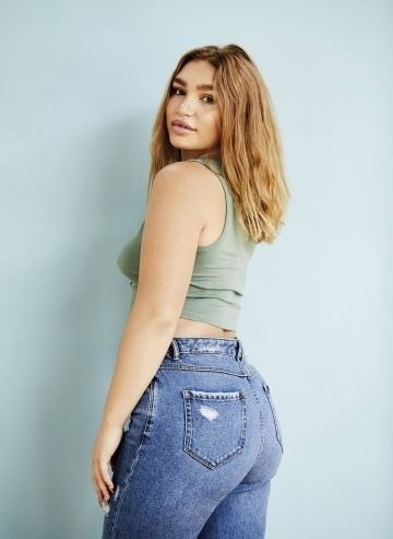Rylee Martell smiling in a backside pose with her blonde hair down and wearing a light green tank top and jeans