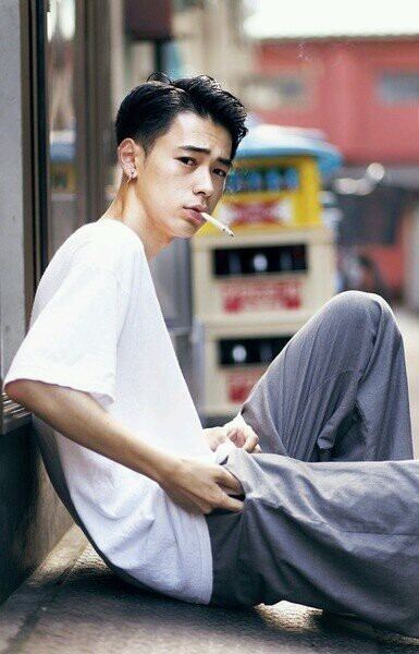 Ryo Narita smoking while sitting on the floor and wearing a white t-shirt and gray pants