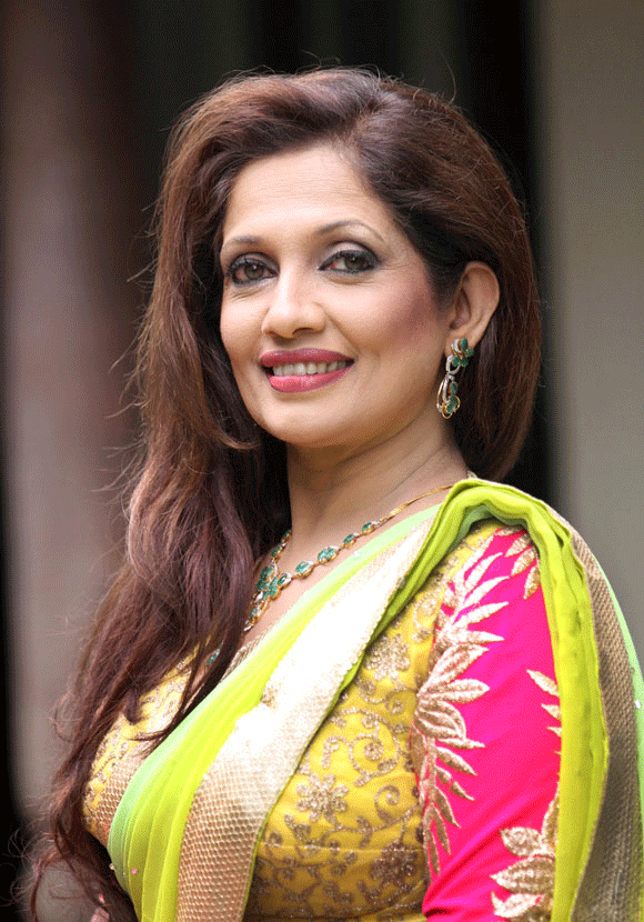 Sabeetha Perera smiling while wearing a yellow and pink dress, gold and yellow dupatta, necklace, and earrings