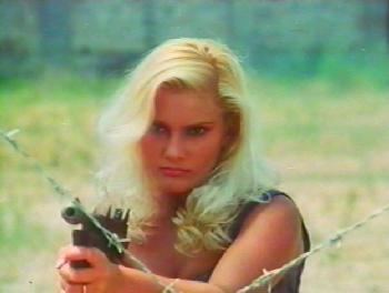 Sabrina Siani as Maida with a fierce look while holding a gun, with wavy blonde hair, and wearing a black sleeveless top in a movie scene from 2020 Texas Gladiators, an Italian science fiction action film.