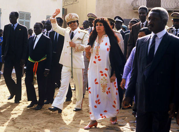 Safia Farkash walking with her then husband, Muammar Gaddafi wearing a white, floral designed dress and a black burka.