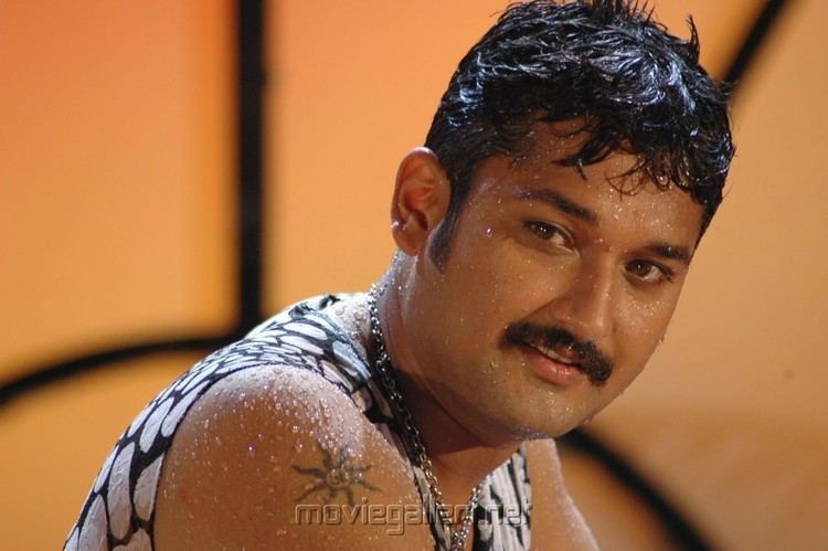 Sai Kiran smiling while wet having a beard and mustache and wearing a black and white shirt and silver necklace