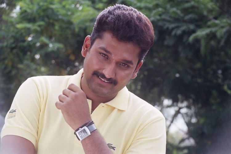 Sai Kiran smiling with a beard and wearing a yellow collared shirt, and wristwatch