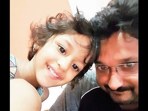 Sai Kiran smiling having a beard and mustache, wearing a gray and black shirt with his daughter Anoushka