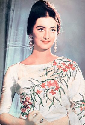 Young Saira Banu smiling and wearing white floral dress and earrings