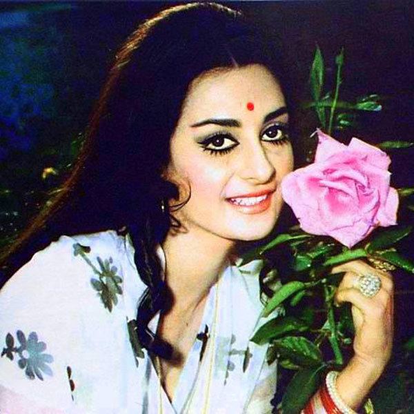 Saira Banu smiling and holding a flower while wearing floral dress