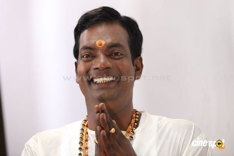 Salim Kumar wearing white shirt and necklace while he is smiling and his hands together