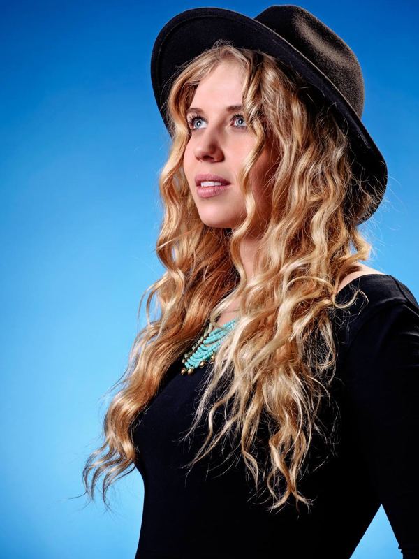 Salka Sól Eyfeld looking afar while wearing a black hat, black long sleeve blouse, and blue necklace