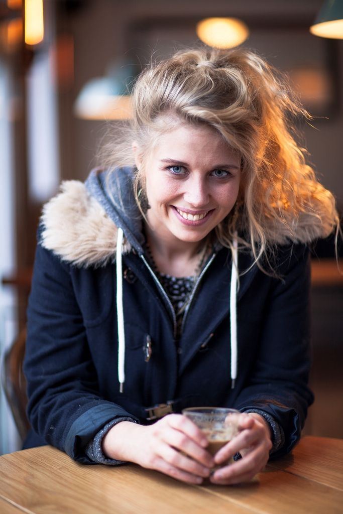 Salka Sól Eyfeld smiling while holding a cup of coffee and wearing a black jacket with fur