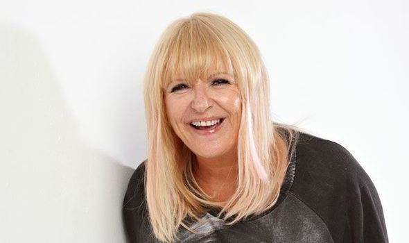 Sally Boazman laughing while wearing a black and gray blouse
