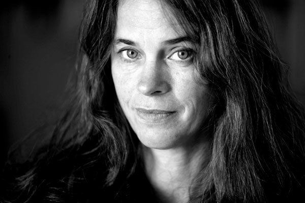 Sally Mann smiling in a black and white background with her hair in a wavy manner.