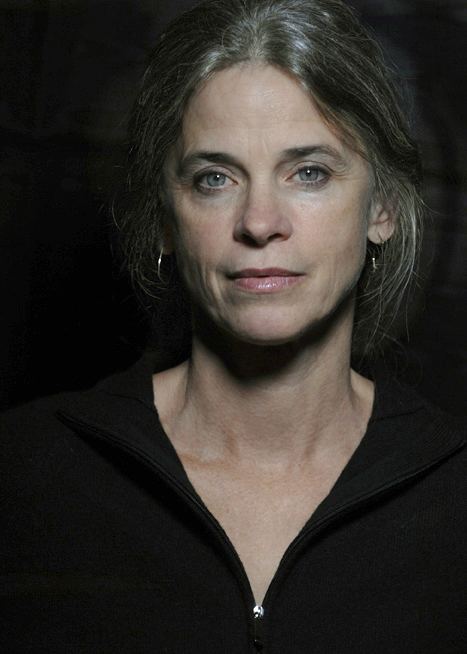 Sally Mann posing with a neutral facial expression and wearing a black shirt and some earrings.