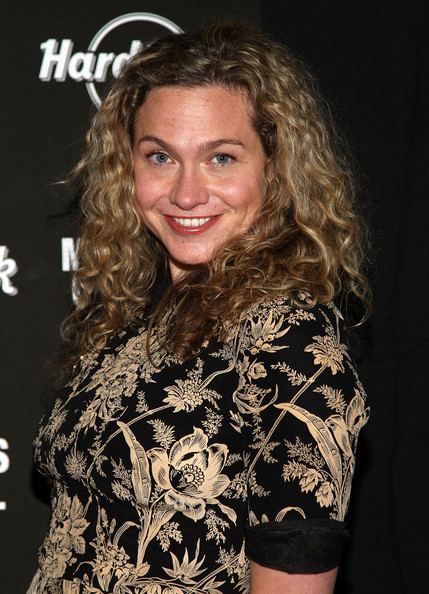 Sally Taylor with a smiling face and curly hair and wearing a floral dress.