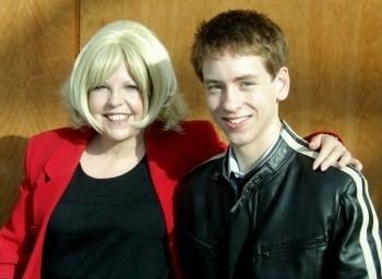 Sally Thomsett and Ciaran Brown are smiling. Sally with blonde hair, wearing a red blazer over a black top while Ciaran wearing a white and black leather jacket.