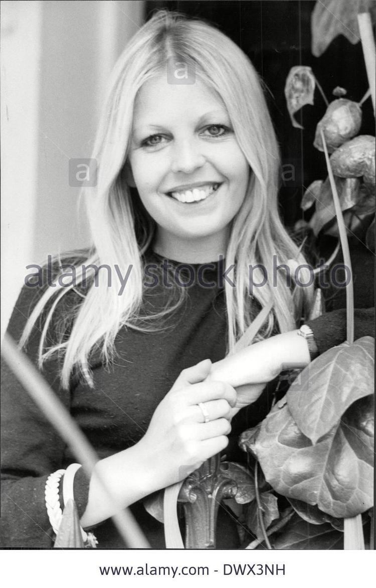 Sally Thomsett smiling while leaning on a fence, with blonde hair, wearing a watch, and a black long sleeve top.