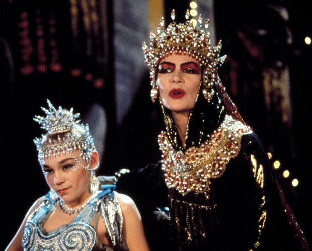 Glenda Jackson talking beside Imogen Millais-Scott while wearing a crown with stones and a black and gold hooded dress in a scene from the 1988 film, Salome's Last Dance