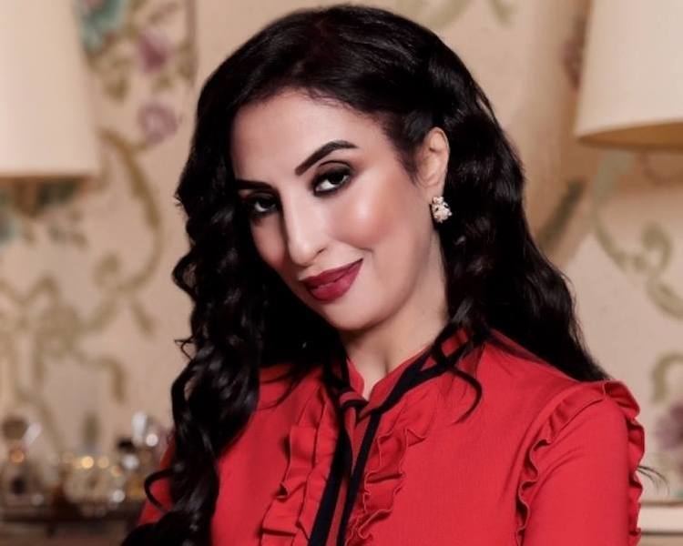 Salwa Idrissi Akhannouch smiling closed mouth while wearing a red dress and sporting curled hair.