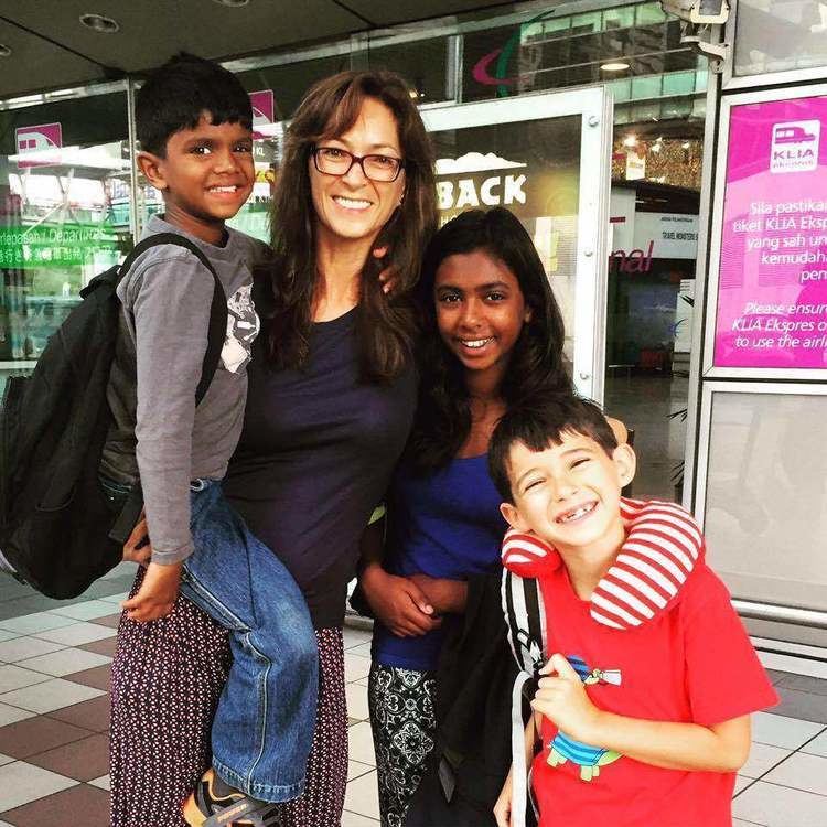 Samantha Schubert wearing eyeglasses and a blue shirt together with her three children.
