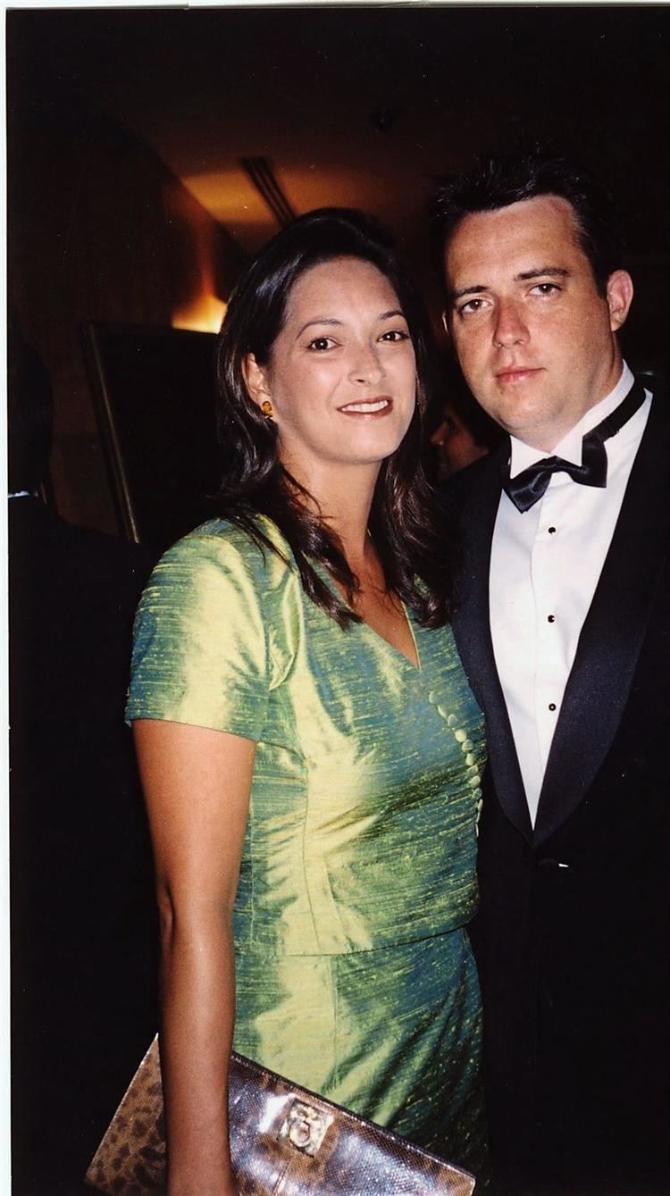 Samantha Schubert wearing earrings, a green dress, and carrying a bag with a man wearing a black suit and bow tie.