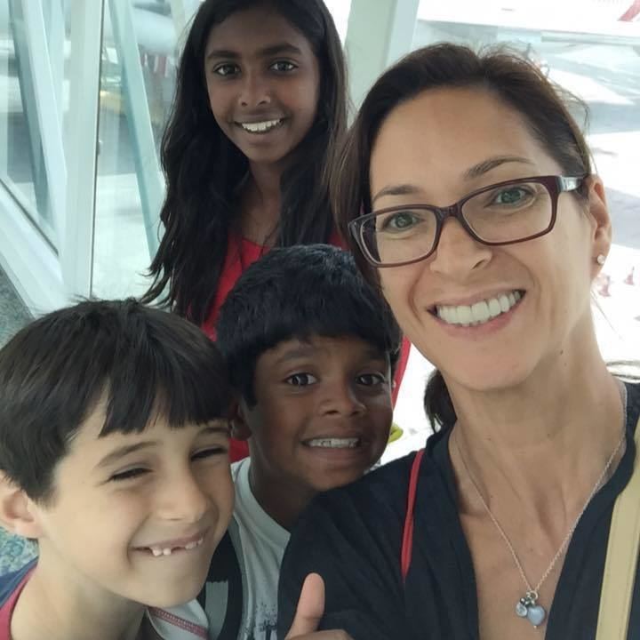 Samantha Schubert wearing eyeglasses, a necklace, and a blue shirt together with her three children.