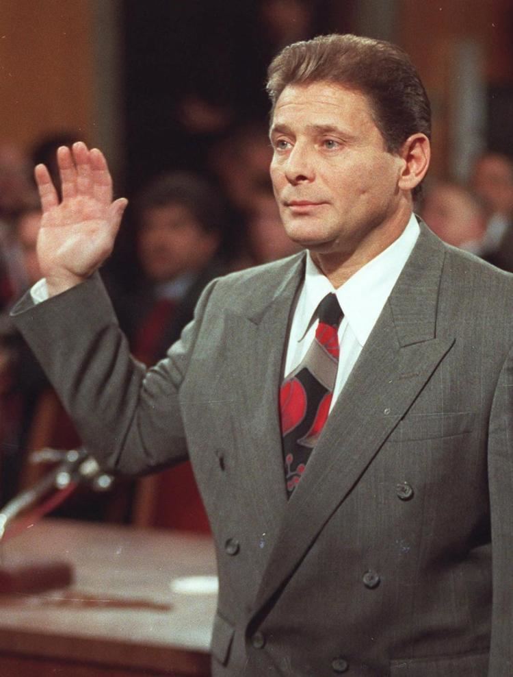 Sammy Gravano raising his hand for the sworn testimony at court wearing a gray suit as well as a black and red tie.