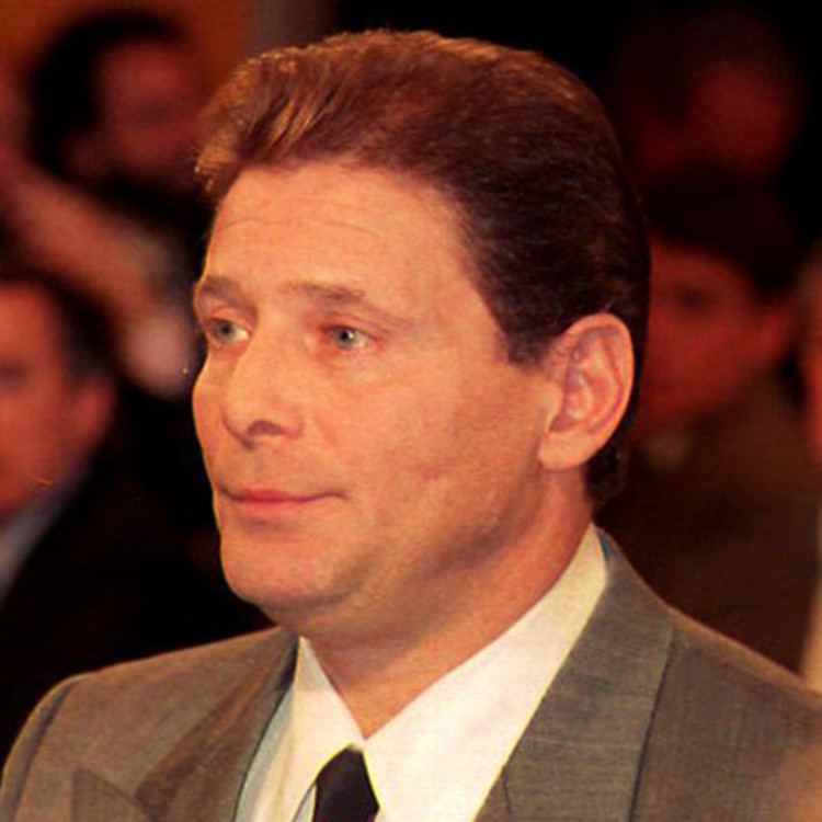 Sammy Gravano raising his hand for the sworn testimony at court wearing a gray suit as well as a black and red tie.