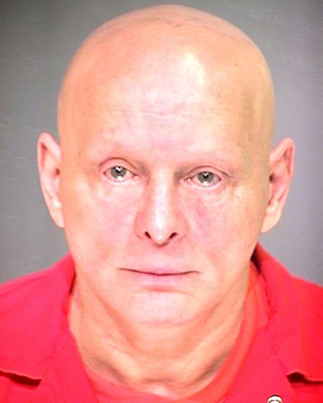 Sammy Gravano posing for his mugshot with his head shaved bald and wearing a red prison attire.