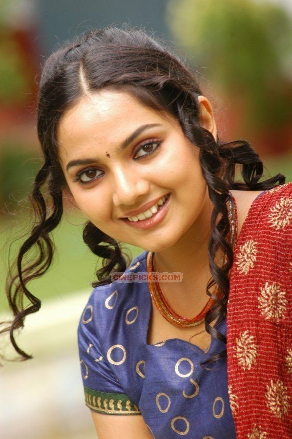 Samvrutha Sunil with a smiling face, curly black hair, wearing a necklace and red, blue, green Indian traditional clothing.