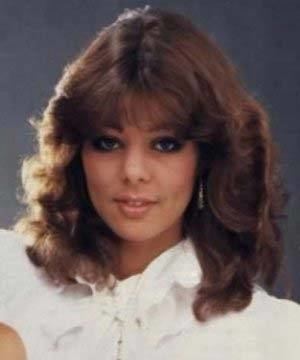 Sandra Ann Lauer is smiling, has brown hair, wearing silver earrings and a white top.