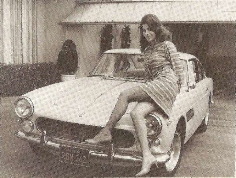 Sandra West sitting in a car and wearing a striped dress and stilletos.