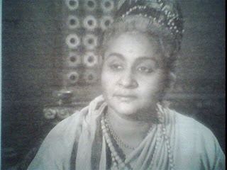 Santha Kumari wearing a headdress, pearl necklace, and dress