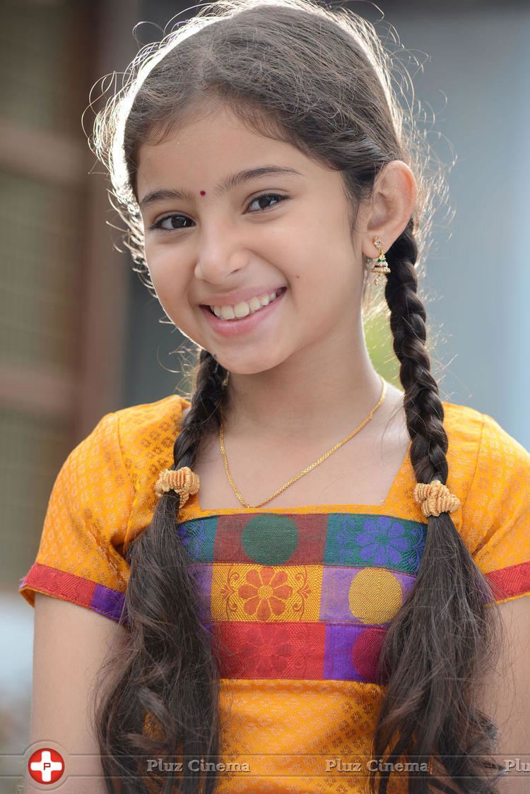 Sara Arjun smiling with her braided hair and a red dot on her forehead while wearing a yellow blouse, necklace, and earrings