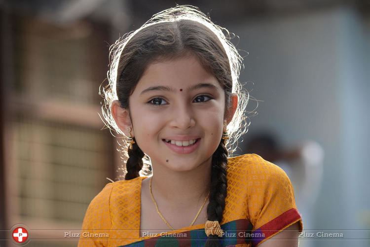 Sara Arjun smiling with her braided hair and a red dot on her forehead while wearing a yellow blouse, necklace, and earrings