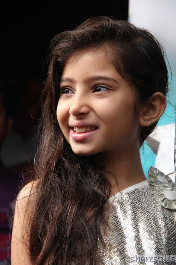 Sara Arjun smiling while looking on the side with her hair down and wearing a gray glossy dress