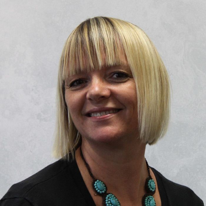 Sarah Ann Kennedy smiling, with short blonde hair, wearing a necklace and a black shirt.