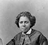 Edmonia Lewis is an American sculptor. Edmonia with a serious face, wearing a black coat over a white top.