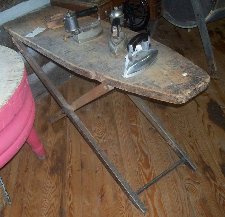 A historic wooden ironing board with flat irons above it.