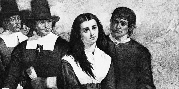 A woman with a sad face surrounded by men during the witch trials in the late 17th century was accused to be a "witch".