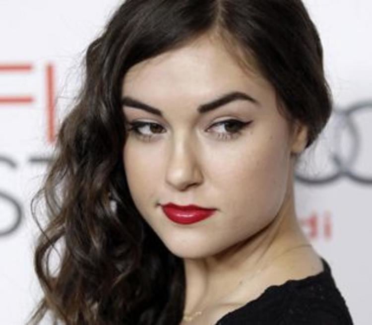 Sasha Grey smiling with her wavy hair down and wearing a black blouse