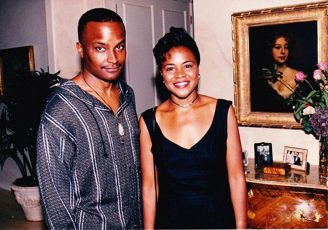 Saundra Quarterman wearing black dress while smiling with a man beside her wearing blue and white long sleeves