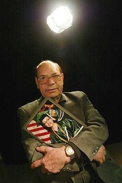 Sayed Bozorg Mahmoody wearing eyeglasses and a suit while holding a picture frame of his daughter.