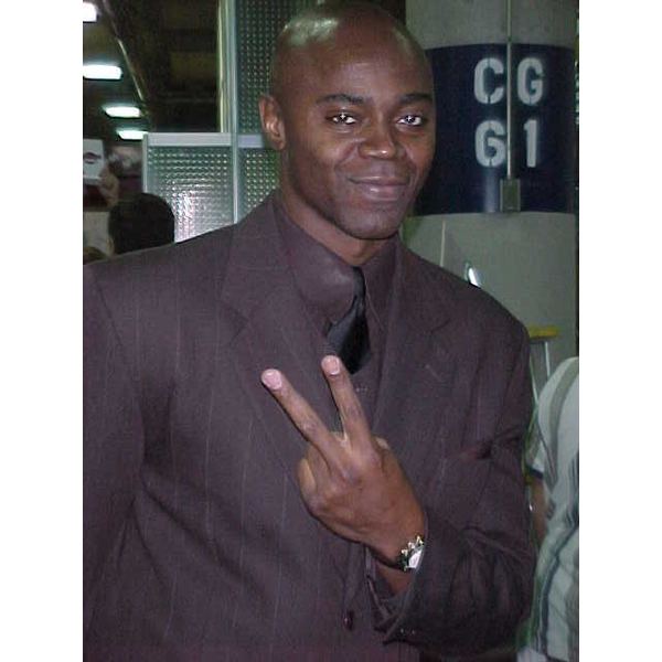 Sean Michaels smiling and wearing a suit and black tie while doing a peace sign.