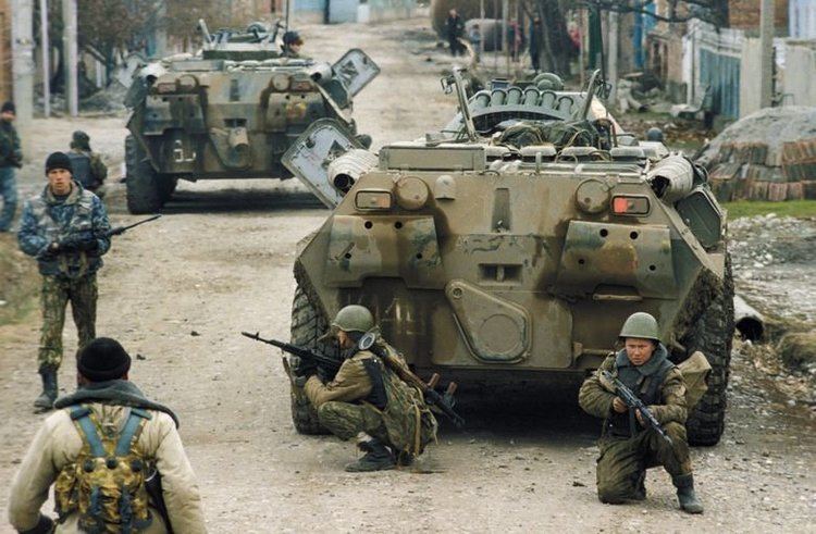 Russian troops are holding their guns and ready to fight while beside them are two tanks during the Second Chechen War