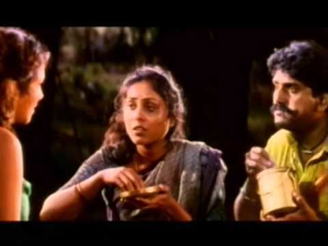 In the movie scene of Seevalaperi Pandi 1994, From left is a woman in front of  Saranya Ponvannan (middle) and Napoleon (right) has short brown hair wearing a green top, in the middle is Saranya Ponvannan is shocked while eating with her right hand to pick up her food and her left hand holding the copper plate, has black curly hair wearing a bracelet and gray Indian clothes, on the right, Napoleon is shocked while eating with his right hand to pick up her food and his left hand holding the wooden cup has mustache and black hair wearing a necklace with white pendant, bracelet, and yellow polo.