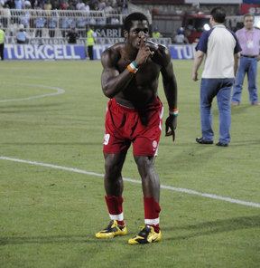 Serge Djiehoua in a football field while wearing red shorts and black and yellow rubber shoes