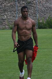 Serge Djiehoua walking in a football field with his red top held by his left hand