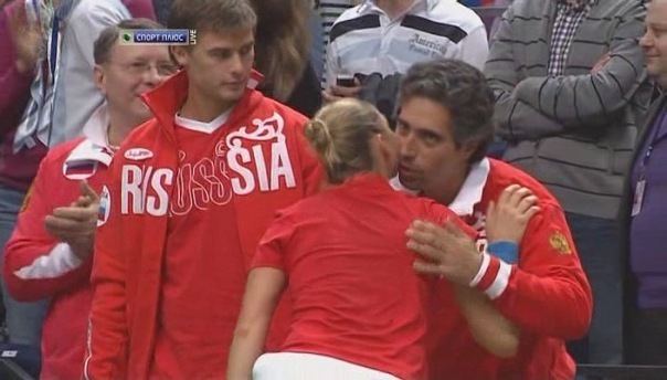 Sergei Demekhine looking at the man beside him kissing a girl while he is wearing a red and white jacket and red t-shirt