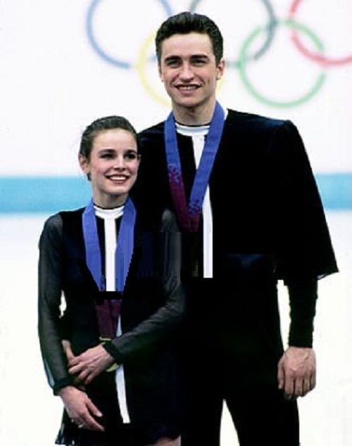 Ekaterina Gordeeva and Sergei Grinkov are smiling after receiving their gold medal at the Winter Olympic Games while Ekaterina wearing a black and white long sleeve dress and Sergei wearing a black and white long sleeve