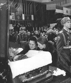 Sergei-Grinkov lying in the coffin while Ekaterina Gordeeva and a woman looking at him and holding his face with soldiers and other people behind them