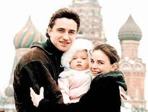 Sergei Grinkov, Dasha, Ekaterina Gordeeva (from left to right) are smiling and hugging each other at Saint Basil's Cathedral while Sergei wearing a brown jacket, Dasha wearing a pink jacket, and Ekaterina wearing a black jacket